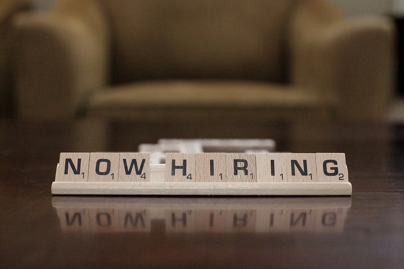 'Now hiring' is spelled out with scrabble cubes placed on a desk. We're hiring an occupational therapist.